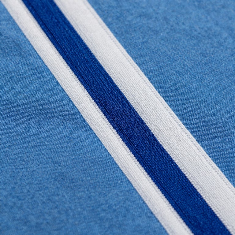 Gros plan macro sur les coutures renforcées d'une blouse médicale en coton tissé Faso Dan Fani bleu et blanc, texture du fil visible sous une lumière de studio précise.