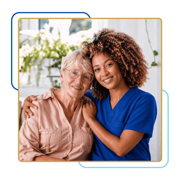 Smiling caregiver in blue scrubs embracing a senior woman, showing compassionate support in a bright home setting