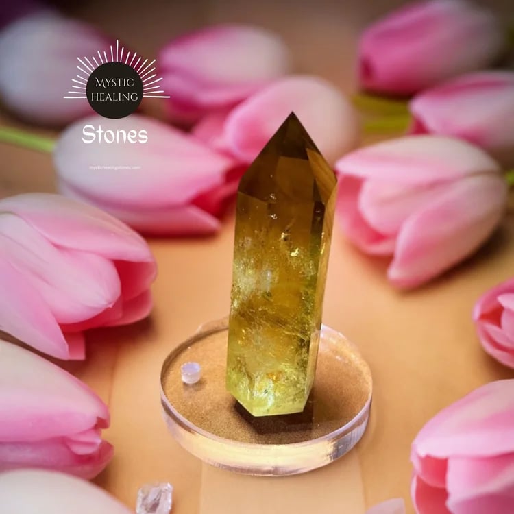 Yellow citrine crystal point for mystic healing surrounded by pink tulips on a neutral background.