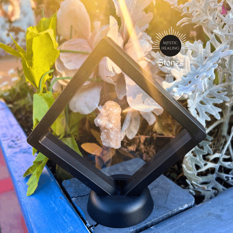 A raw fairy amethyst displayed in a black 3D floating frame outdoors among flowers.