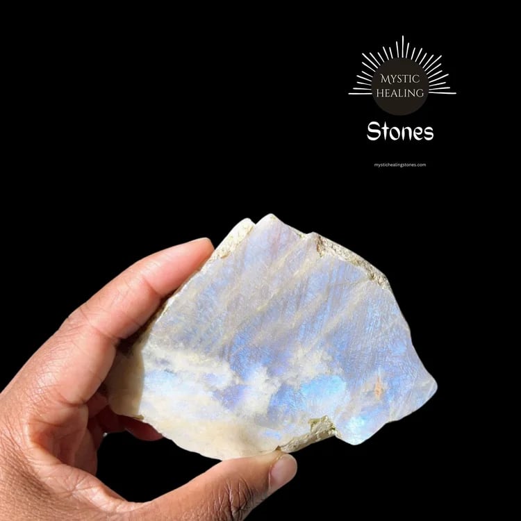 Hand holding a raw moonstone crystal with blue flash adularescence for mystic healing.