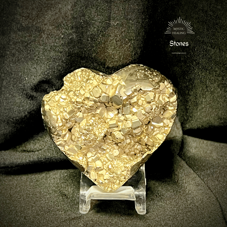 Heart-shaped raw pyrite crystal cluster on a clear display stand against a dark fabric background.