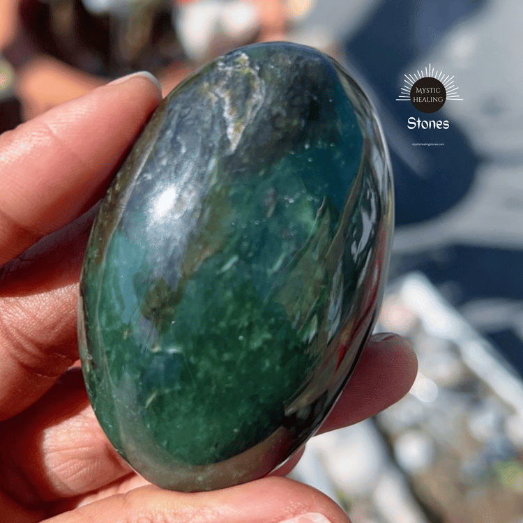 A hand holding a polished green jade palm stone crystal for healing.