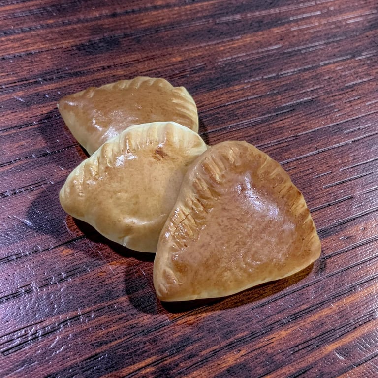 Golden brown baked empanadas with crimped edges on a dark wood grain table.