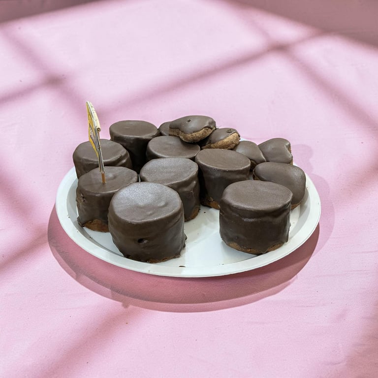 A white plate filled with gourmet chocolate covered marshmallows on a pink background.