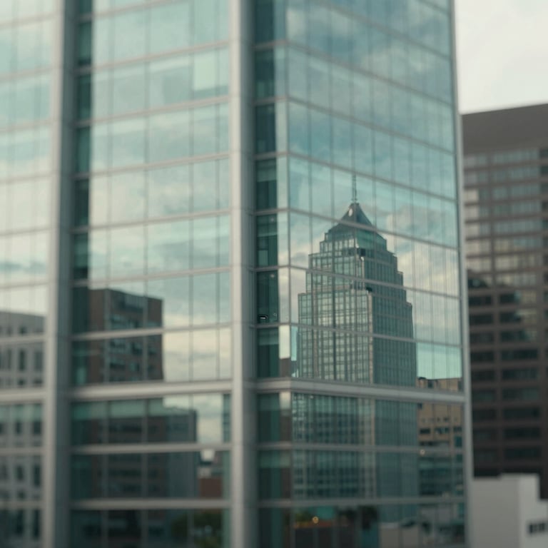 A wide shot of a modern city skyline reflecting in the windows of a corporate building, featuring cool sage tones (#A2B9B8).