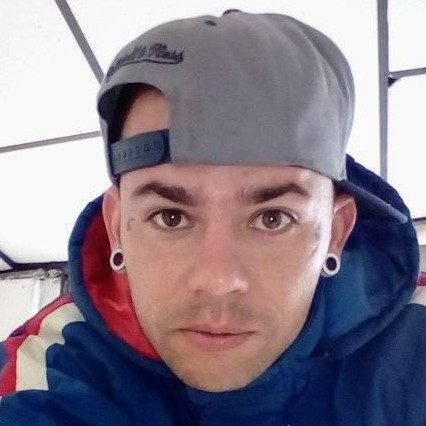 Retrato de un hombre con una gorra gris tipo snapback, sudadera azul con capucha y dilataciones 