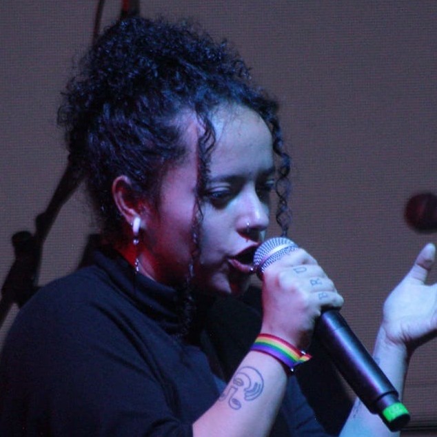 Cantante femenina de cabello rizado interpretando en vivo en el escenario con un micrófono 