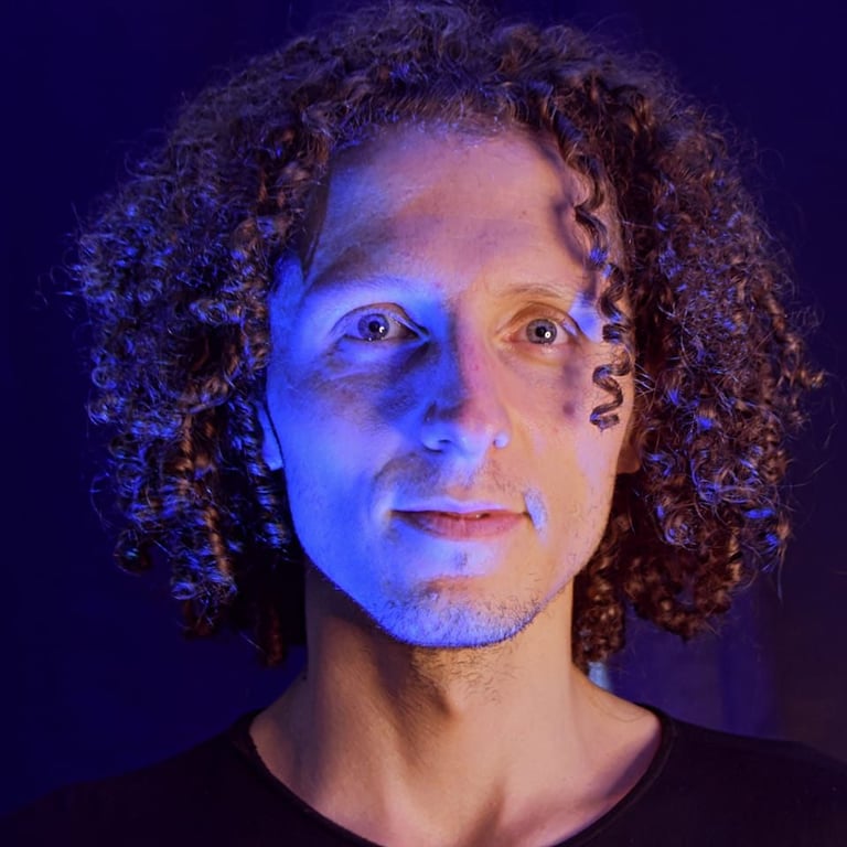 Retrato de un hombre con cabello castaño rizado, iluminado con una dramática luz de estudio azul y c