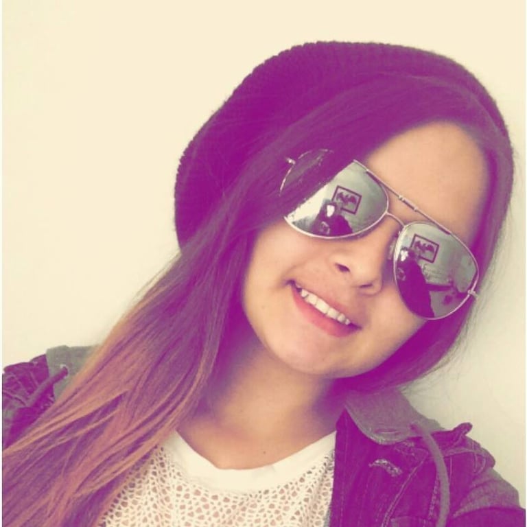 Joven sonriente con un gorro negro y gafas de sol plateadas tipo aviador, en un retrato moderno 