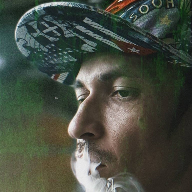 Un hombre con una gorra de béisbol estampada exhala una densa nube de humo en una vista de perfil 