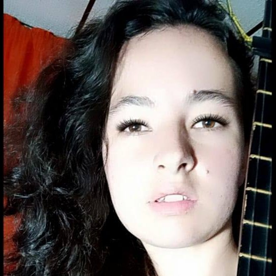 Una joven con cabello largo, oscuro y ondulado, posando de cerca junto al diapasón de su guitarra 