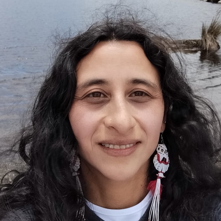 Una mujer sonriente con cabello largo, rizado y oscuro, usando aretes artesanales de macramé 