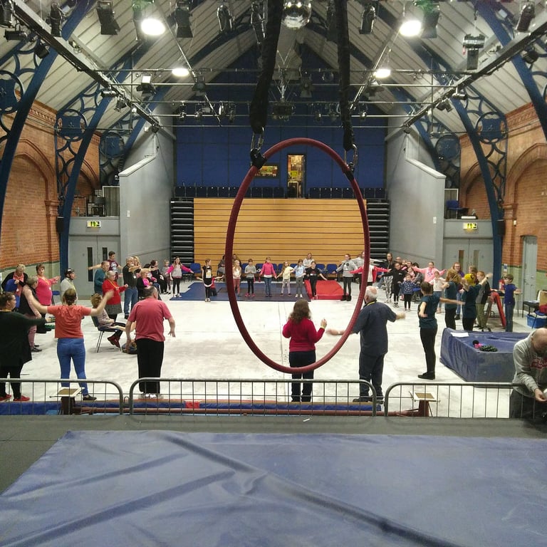 Students practicing aerial arts and circus skills in a large training hall with a red hoop.