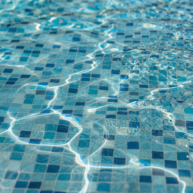 Detail of luxury mosaic pool tiles shimmering under water with sunlight reflections.