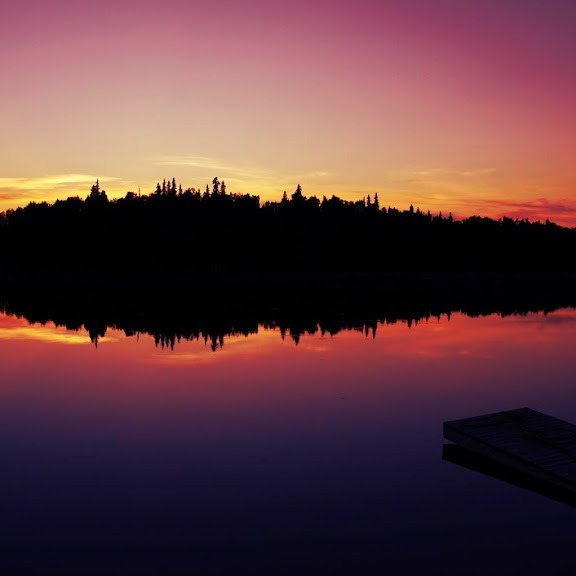 photo: reflection of fiery sunset and trees on a placid lake in Alaska