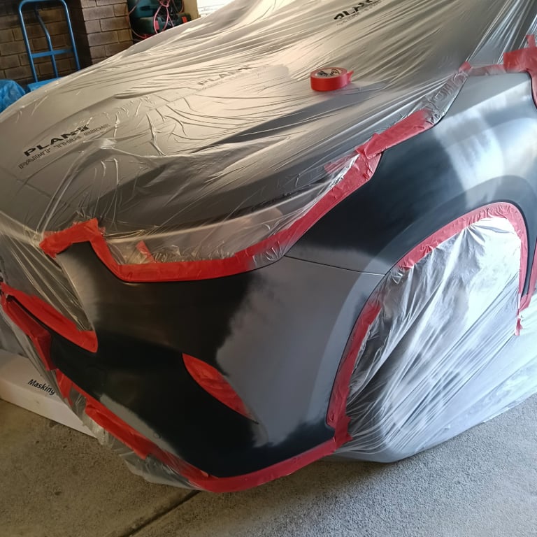 Professional car body repair with plastic masking and red tape for automotive painting.