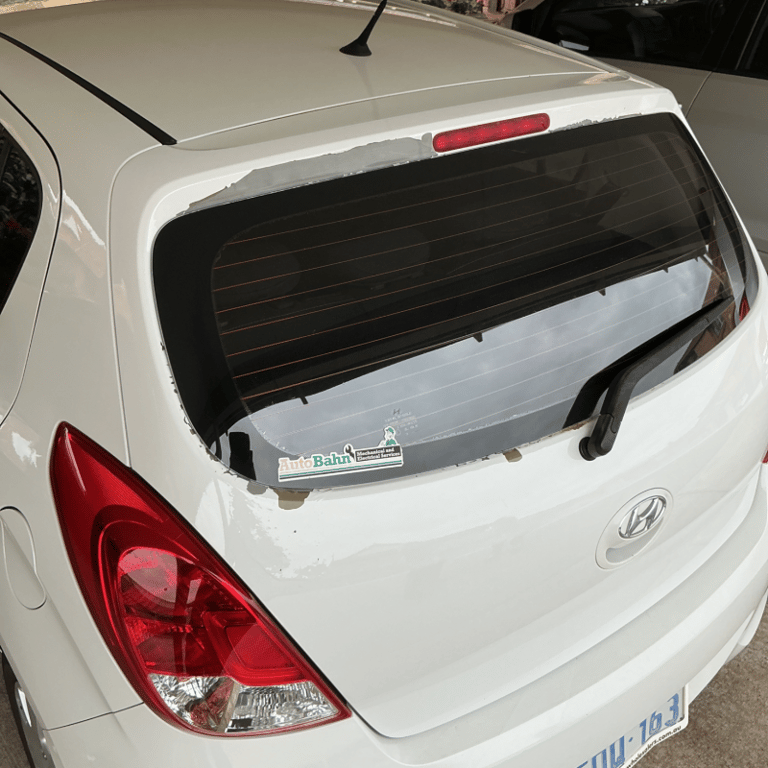 Rear view of a white Hyundai hatchback showing peeling clear coat paint damage around the back window.