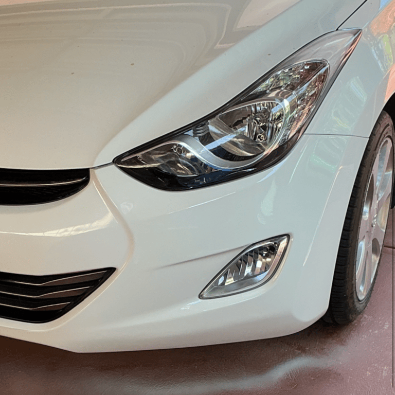 Close-up of a white sedan front bumper featuring sleek headlights and integrated fog lamps.