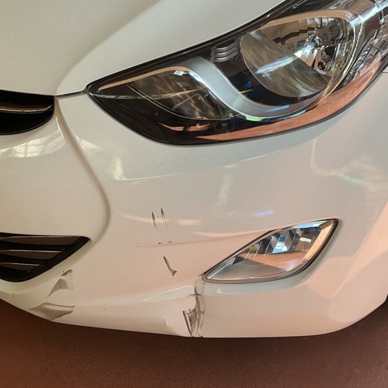 Close-up of a white car's front bumper showing minor collision damage, paint scratches, and a dent