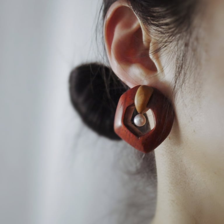 Handmade wooden geometric earring with a white pearl accent worn on a person's ear.