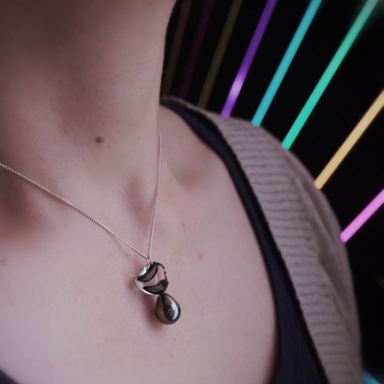 Elegant black pearl pendant on a silver chain necklace worn against a vibrant neon light background.
