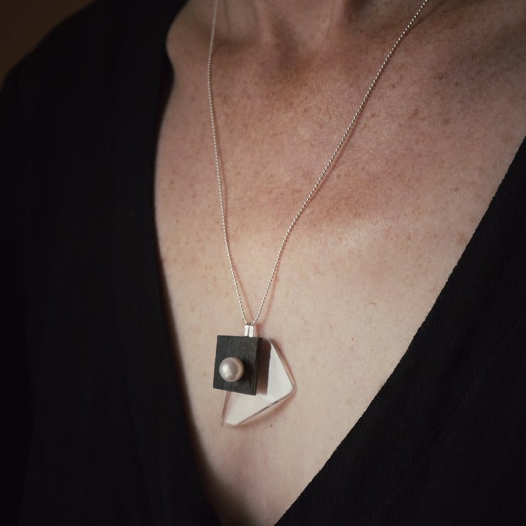 A modern geometric pendant necklace with silver chain, ebony wood, acrylic, and a pearl.