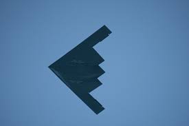 A black B-2 Spirit stealth bomber aircraft flying against a clear blue sky background.