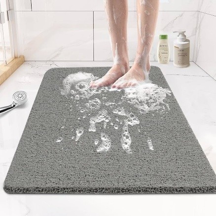 a person standing on a non-slip bathroom rug with a shower head and soap on the mat