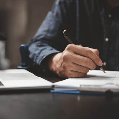 a man is writing on a notebook and holding a pen