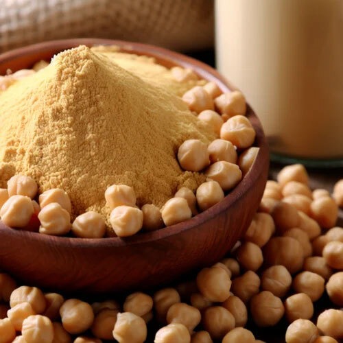 Finely ground chickpea flour in a wooden bowl surrounded by whole dried garbanzo beans.