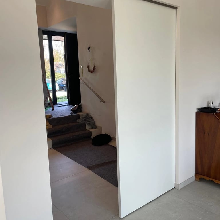 Drzwi przesuwne w ścianie g-k prowadzące do salonu z dużymi oknami.