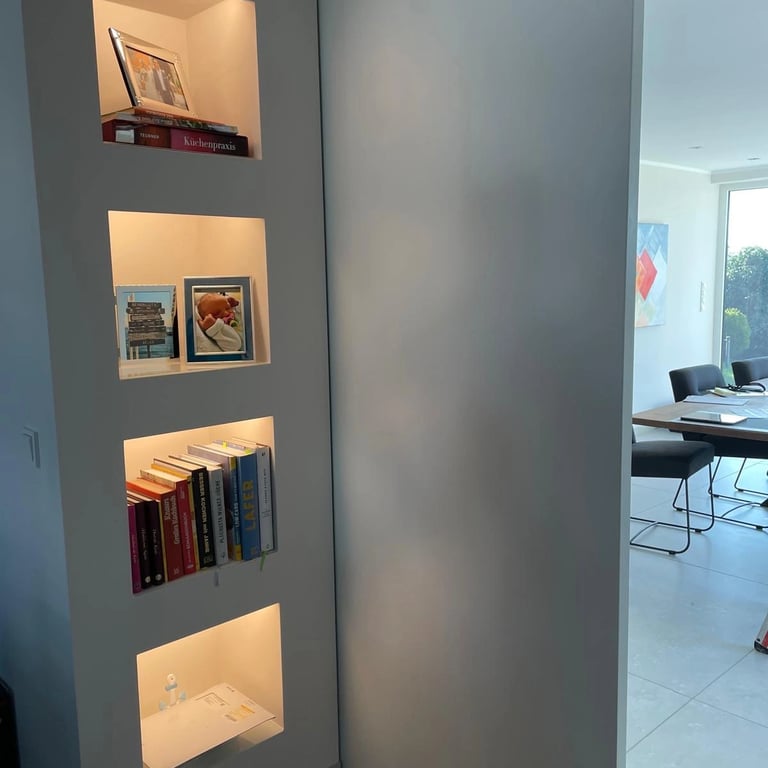 Drzwi przesuwne w ścianie g-k z zabudową i podświetlanymi półkami LED.