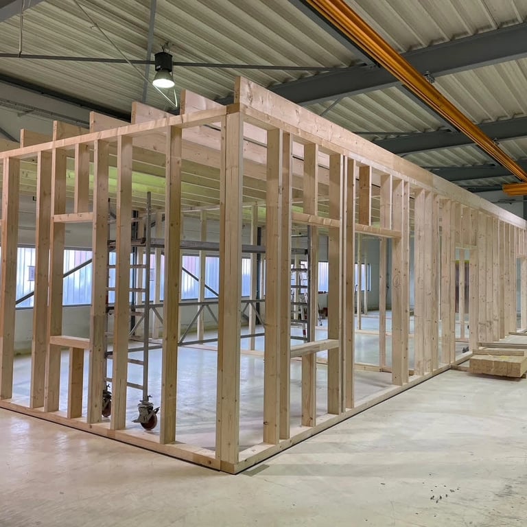 Konstrukcja drewniana ścian działowych w hali, widoczne profile z drewna, otwory na drzwi i okna, jasna betonowa posadzka i s