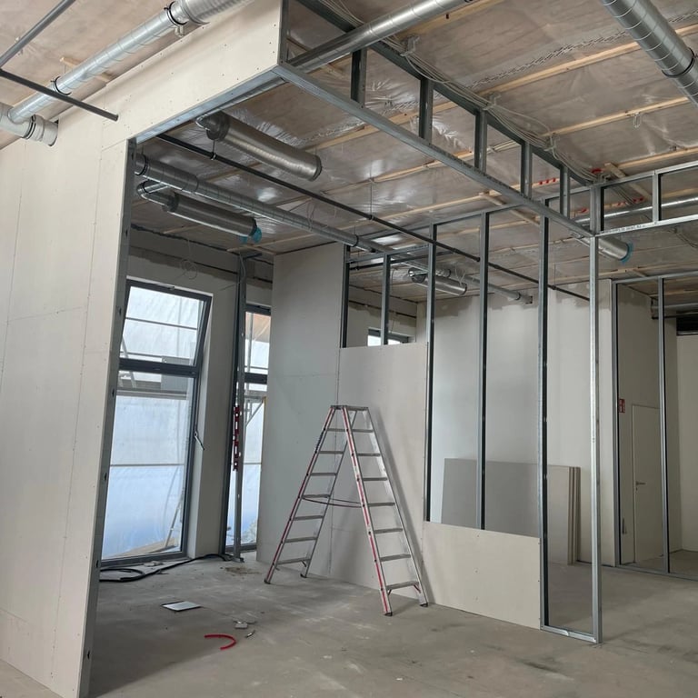 Konstrukcja ściany działowej z profili metalowych w biurze, widoczne drabiny i instalacje.