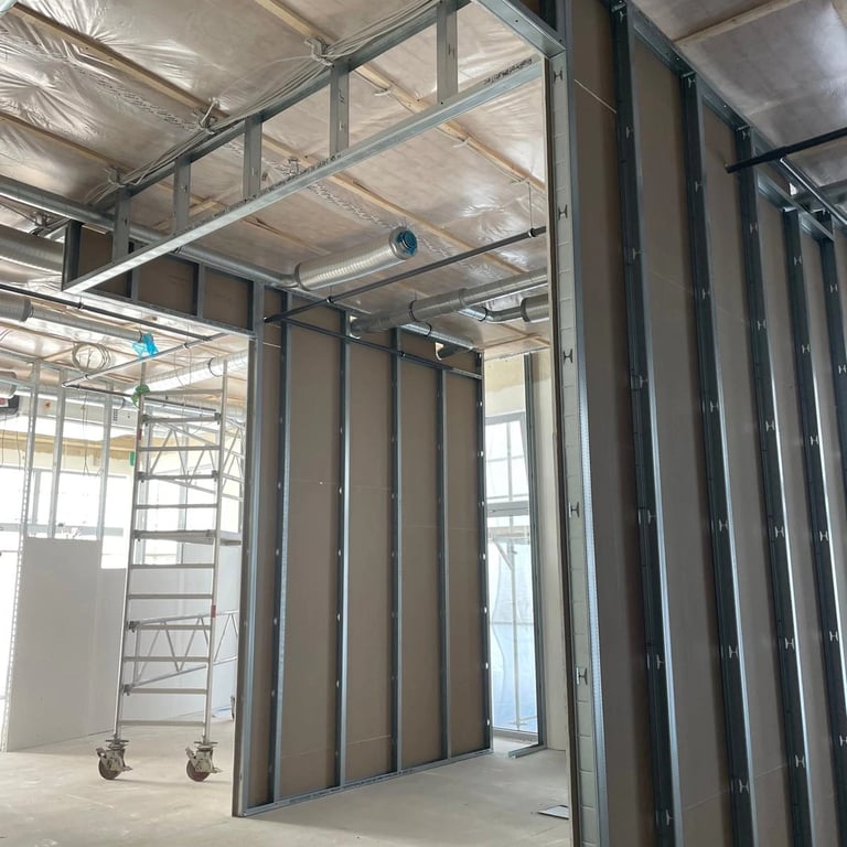 Konstrukcja ściany działowej z profili metalowych, widoczne rusztowanie i izolacja pod sufitem.
