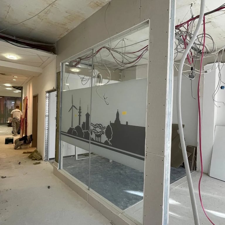 Montaż ściany działowej z przeszkleniem, widoczne przewody elektryczne i profile metalowe.