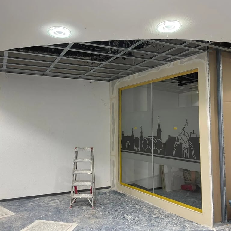 Montaż ściany działowej z dużym oknem, widoczne profile metalowe i szpachlowanie.