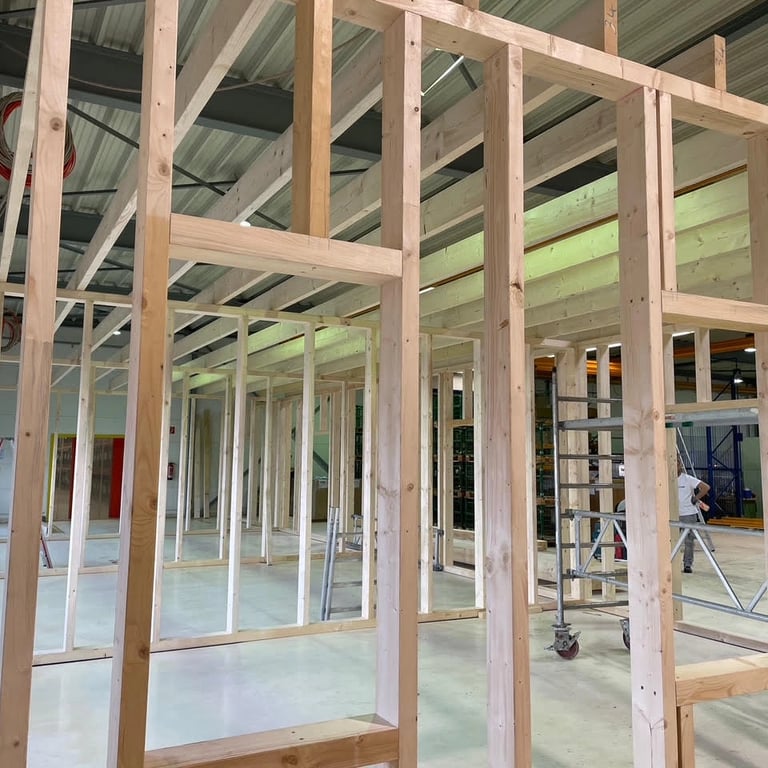 Montaż ścian na konstrukcji drewnianej w dużej hali przemysłowej, widoczne drewniane belki, otwory na drzwi i okna, metalowy 