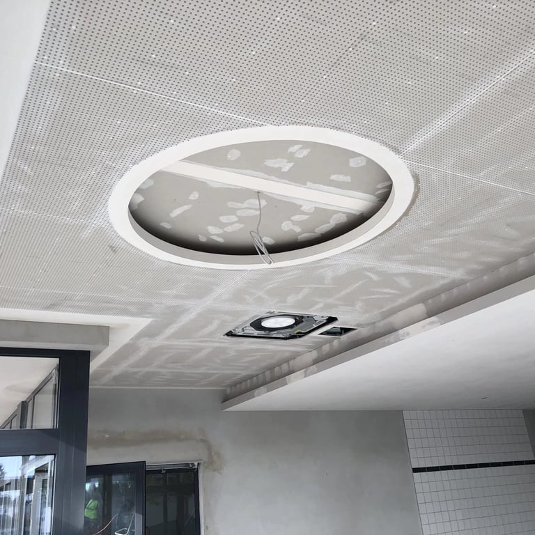 Montaż sufitu akustycznego z perforowanych płyt gipsowych, widoczne otwory na instalacje i okna w tle.