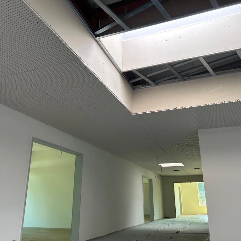 Zabudowa sufitu akustycznego z perforowanych płyt, widoczne otwory na instalacje i przygotowanie pod malowanie.