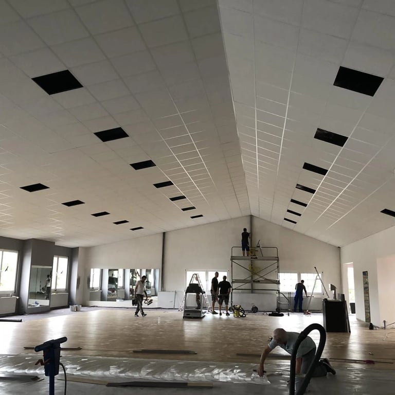 Sufit kasetonowy w trakcie instalacji, widoczne panele, izolacja akustyczna i przewody elektryczne w konstrukcji.