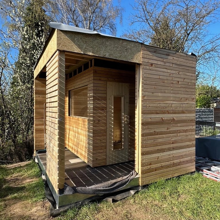 Wnętrze sauny z drewnianymi ścianami i sufitem, jasne deski, okno poziome i podłoga wyłożona płytkami ceramicznymi.