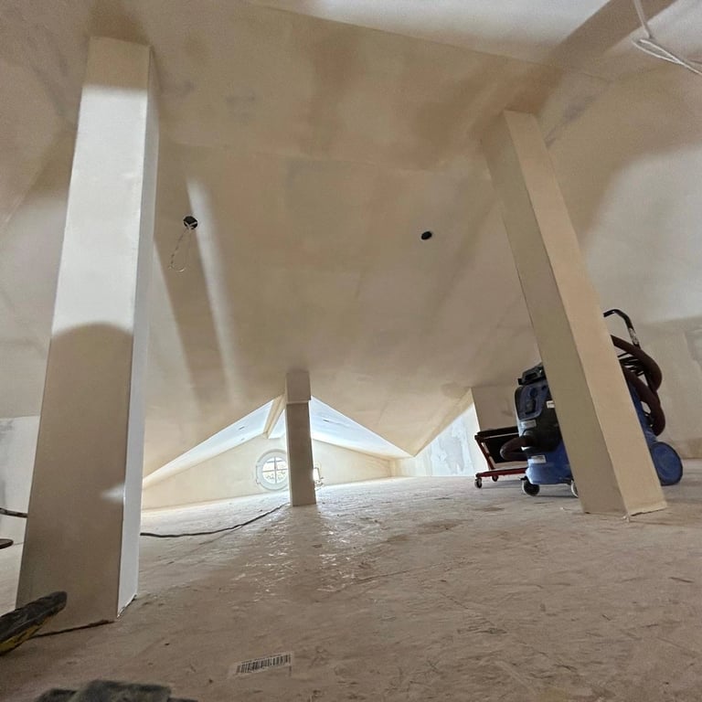 Zabudowa poddasza z płytami gipsowo-kartonowymi, widoczne słupy konstrukcyjne, instalacje elektryczne i przygotowanie do szpa