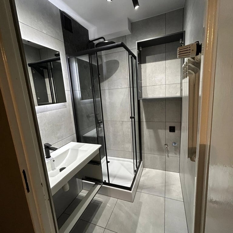 Łazienka z prysznicem w szklanej kabinie, jasnoszare płytki i nowoczesne oświetlenie sufitowe.