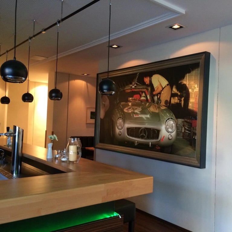 Zabudowa baru z drewnianym blatem, podświetleniem LED i dekoracyjnym obrazem w dużej ramie, nowoczesne lampy wiszące.