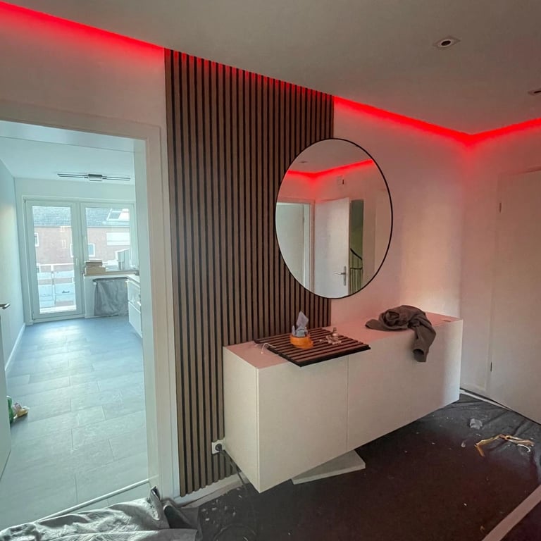 Zabudowa w holu z lamelami drewnianymi na ścianie, okrągłym lustrem i czerwonym podświetleniem LED na suficie.