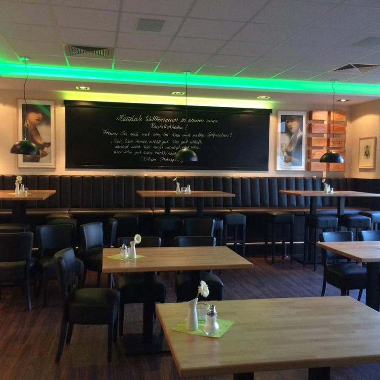 Zabudowa w restauracji z podświetlanym sufitem LED w kolorze zielonym, drewniane stoły i czarne krzesła w nowoczesnym układzi