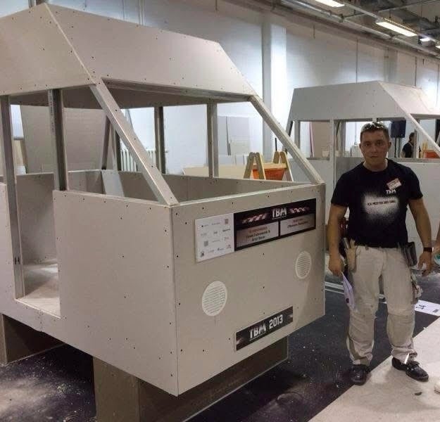 Zabudowa ściany z lamelami drewnianymi, drzwi z szybą matową, nowoczesne wnętrze z oświetleniem sufitowym.