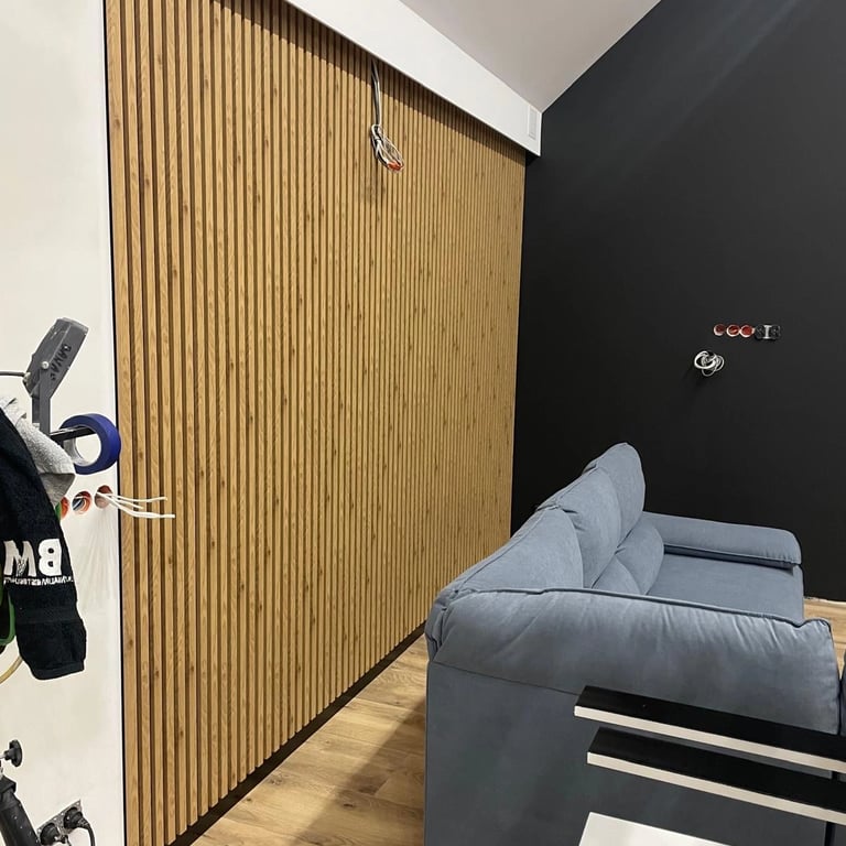 Zabudowa ściany z pionowymi lamelami drewnianymi w salonie, obok ustawiona sofa w kolorze szarym.
